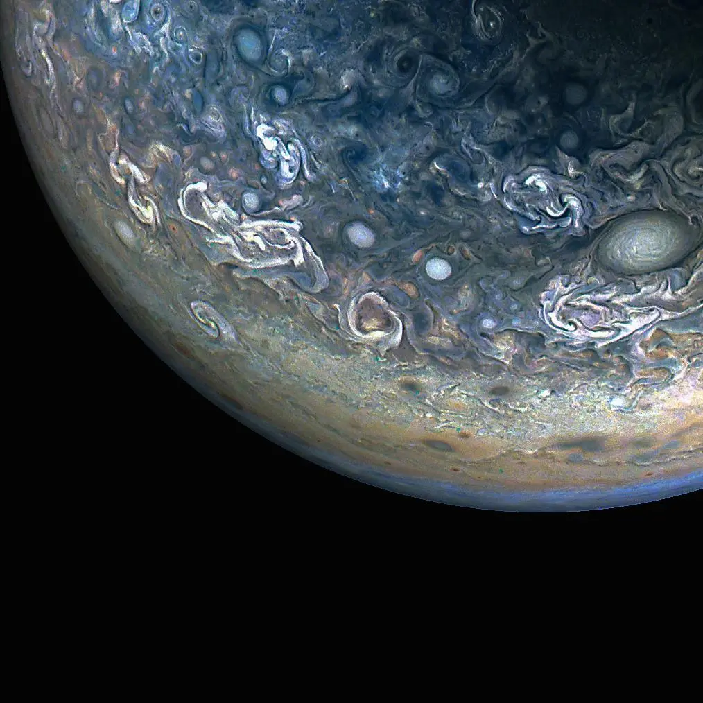 Three quarters of Jupiter can be seen in this photo; the darkness of space covers the bottom of the image. Green and blue swirls cover the planet's surface.