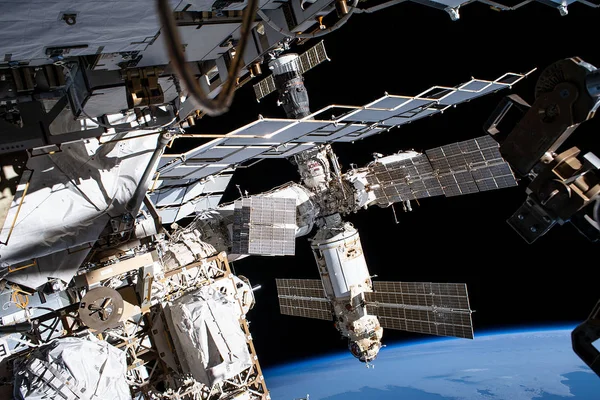 A series of modules and solar panels orbit in space above the curve of Earth’s horizon.