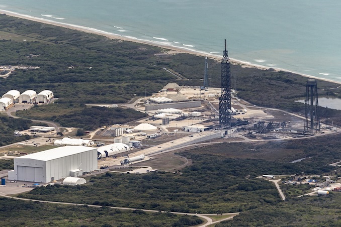 An aerial view of launch complex 36 at the Cape Canaveral Space Force Station showing the aftermath of the New Glenn explosion last Thursday. The rocket itself virtually disintegrated in the blast leaving its transporter-erector in wreckage on the concrete pad’s surface. The large gantry suffered structural damage near its base while the mangled remains of a lightning tower are visible to the right of the pad surface. A large processing hangar (at left) came through the blast without major damage, as did propellant tanks and distribution systems. Image: Adam Bernstein/Spaceflight Now